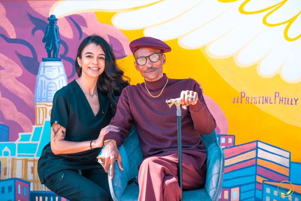 Caregiver smiling while taking a picture in front of Pristine’s mural with their happy care receiver